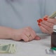 Female Senior Hands Counting Cash Money with Medications Pills on Table