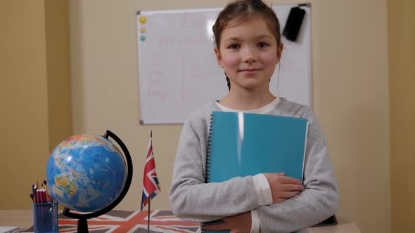Portrait of Schoolgirl with a Notebook at School Near the Blackboard and a Globe alt