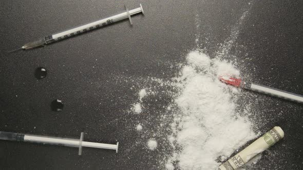 Heroin powder falls on a black table with syringes