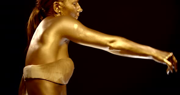 Sexy Woman Is Covered By Shiny Gold Paint Is Dancing, Standing Back To Camera, Medium Shot alt