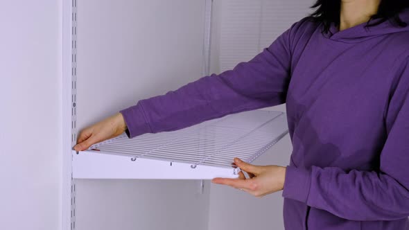 Installation of a metal mesh shelf in the dressing room system on a bracket. A woman in a purple hoo alt