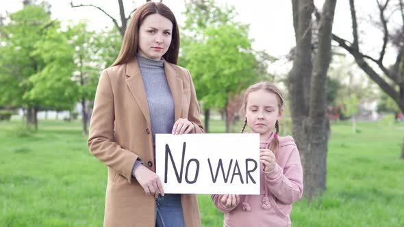 A girl with her mother is holding a banner with the inscription text "No to war". alt