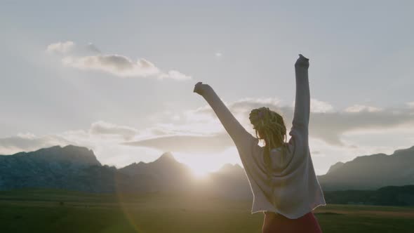 Happy woman with dreadlocks jumping and having fun in Field under sunlight in evening. alt