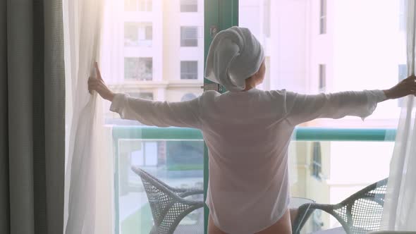 Woman with a Towel on the Head After a Shower Opens the Curtains at Hotel Window