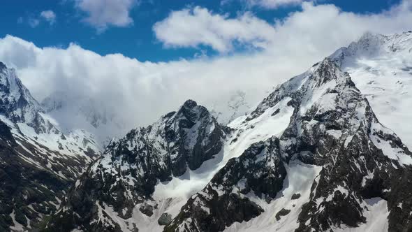 Air Flight Through Mountain Clouds Over Beautiful Snowcapped Peaks of Mountains and Glaciers alt