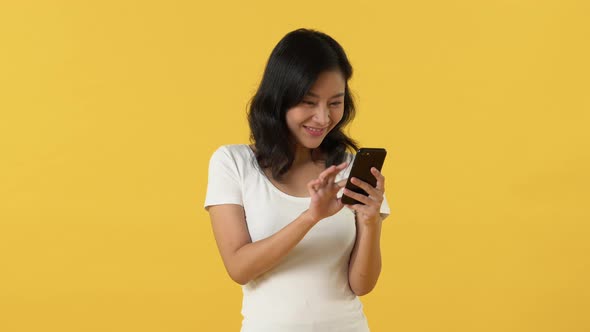 Excited smiling Asian young woman feels overjoyed by reading text messages on cellphone