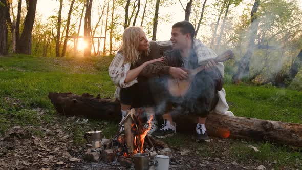 Closeup portrait of a couple sitting with guitar near bonfire in the forest alt