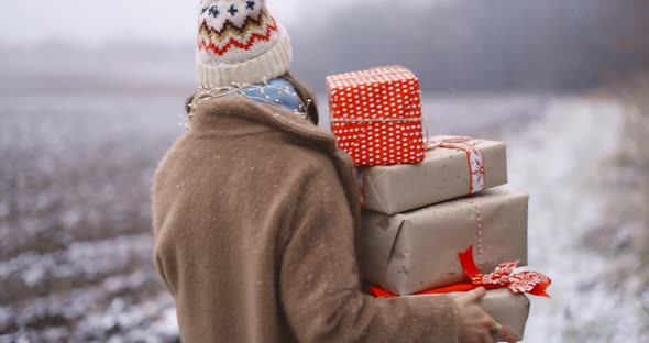 Portrait of a Happy Woman with Gift Boxes on the Snowy Field alt