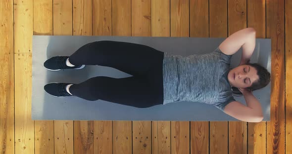 Fat Lady Does Crunches Lying on Mat on Wooden Floor alt