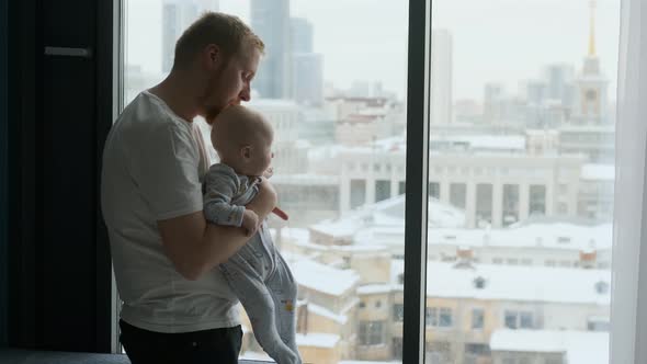 father and baby son look out the window at the city