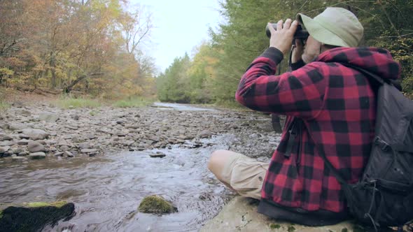 An older hiker resting by a creek in a scenic forest in the mountains. alt
