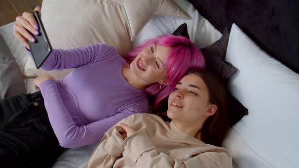 Carefree Woman and Female Friend with Birth Anomaly Making Selfie in Bed alt