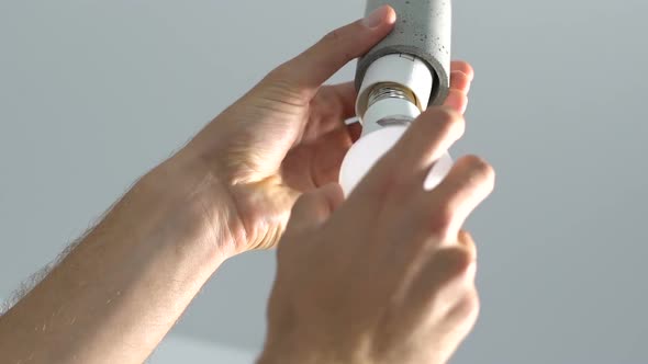 Male hands screwing electricity bulb into switch lampholder alt