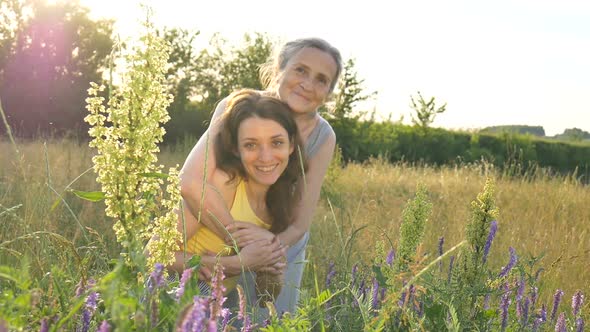 Senior Mother with Gray Hair with Her Adult Daughter Looking at the Camera in the Garden and Hugging alt