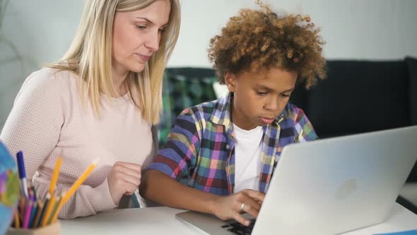 African American Boy Is Sitting at Desk and Browsing Information From New Digital Technology alt