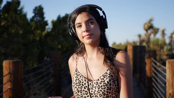 Beautiful young hispanic woman listening to music on her headphones and smartphone while smiling and alt