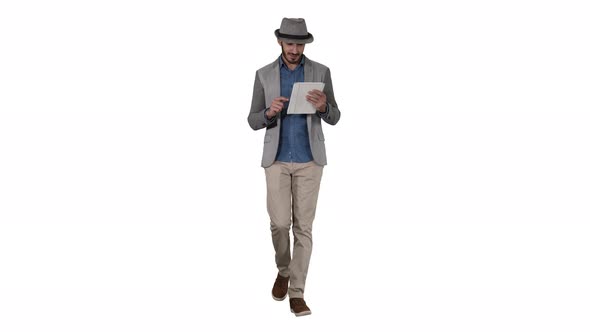 Handsome Smiling Arab Man in a Hat Walking and Using Tablet on White Background alt