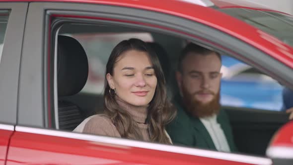 Young Brunette Caucasian Woman with Brown Eyes Closing Car Door and Talking To Blurred Man Sitting alt