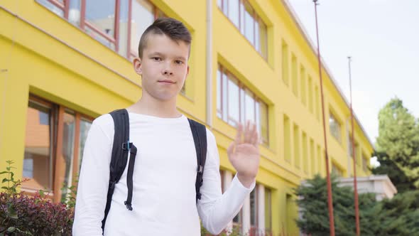 A Caucasian Teenage Boy Waves at the Camera with a Smile  View From Below  a School