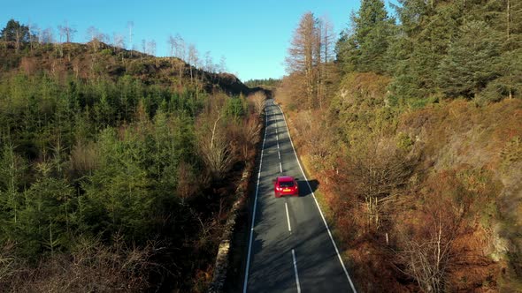 Aerial view of a red car on countryside road through the wood in Wales