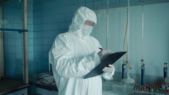 A medical worker in a protective suit and glasses holds a folder with documents