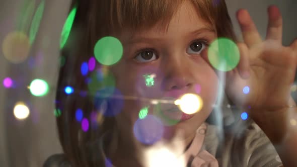 Girl Looks at Camera Through Transparent Ball of Glowing Multicolored Lights