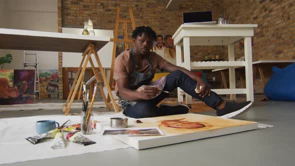Portrait of smiling african american male artist wearing apron painting on canvas at art studio alt