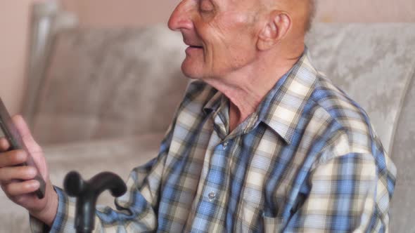 cheerful smiling pensioner caucasian 70-79 years old with a walking stick sits at home and uses a sm alt