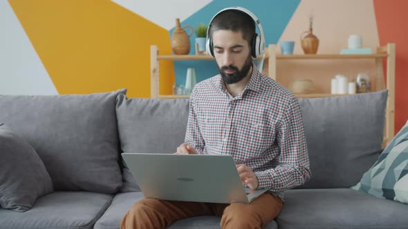 Attractive Arab Guy Using Laptop Computer Typing Listening To Music Through Headphones alt