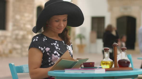 Young Female Writer Making Notes in Notebook, Enjoying Rest in Outdoor Cafe alt