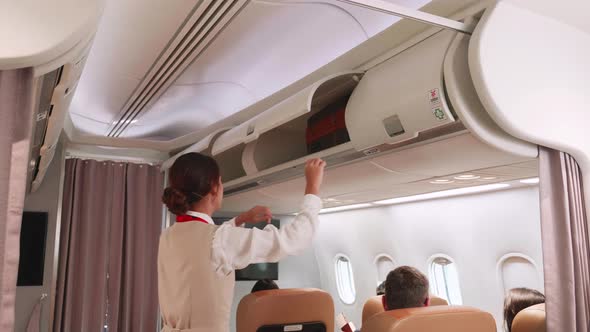 A stewardess closes luggage compartments overhead on aircraft.
