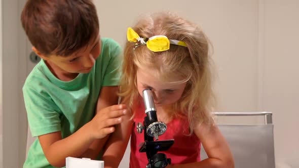 Little Boy is Showing a Cute Little Girl How to Look Through a Microscope Lens alt