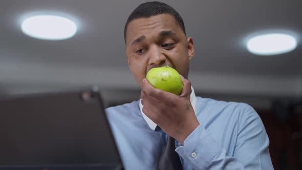 Portrait of Interested Young African American Man Eating Apple Shaking Head Yes Listening to alt