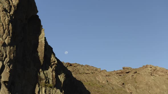 Time lapse of moon rising in sky behind mountains alt