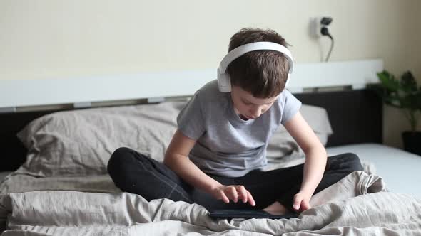 child boy sitting on bed with pc tablet with wireless headphones