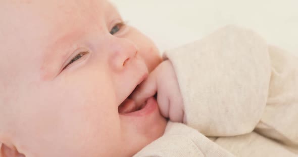 Portrait of a Cute Baby with a Finger in His Mouth in the White Clothes Smiling