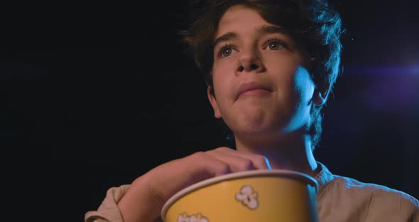 Cute boy watching a movie at the cinema and eating popcorn, entertainment concept