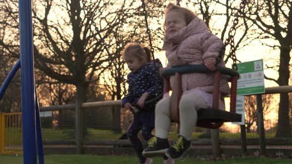 Medium Plan Portrait of Two Cute Little Siblngs Having Fun Swinging On Swing Outside alt