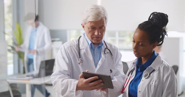 Multiethnic Male and Female Physicians Tapping and Scrolling on Digital Tablet alt