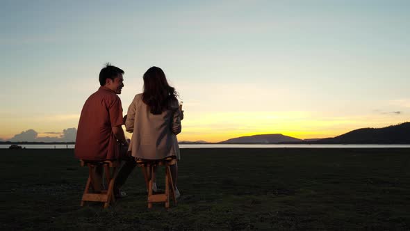 cheerful couple in love talking and sitting at the grass filed at sunset