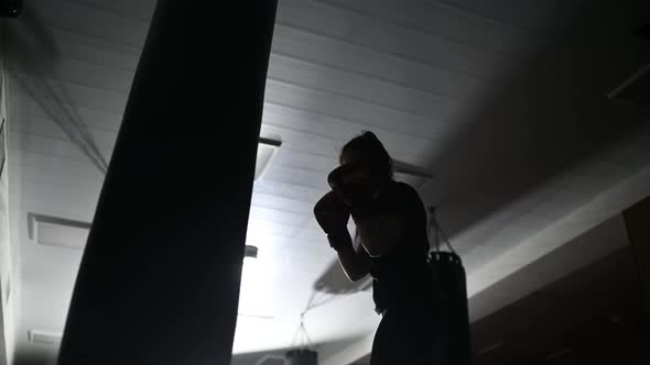 Dark Silhouette of a Boxer Girl Practicing Punches on a Boxing Bag alt