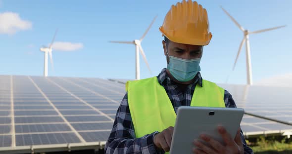 Young man working with digital tablet while wearing safety mask at wind farms alt