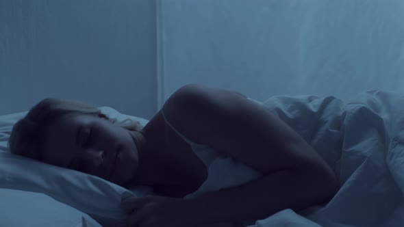 Young woman lying in the bed at night. Beautiful sleeping girl. Twilight in the bedroom. alt