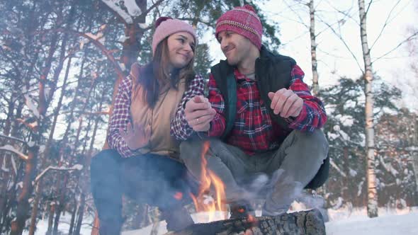 a Pair of Young People in Red Shirts in the Woods Warm Their Hands By the Fire a Winter Picnic alt
