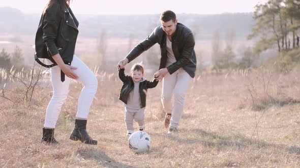 Happy Parents and a Cute Son Are Playing Football Outside alt