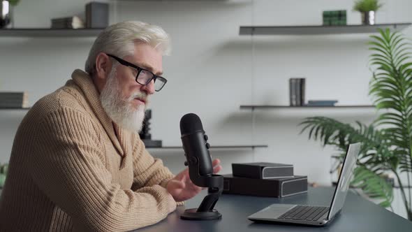 Elderly Man with a Gray Beard Video Blogger Speaking in Microphone. Aged Broadcaster Lives in a alt