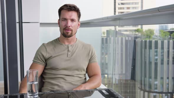 A Young Handsome Man Talks To the Camera As He Sits on a Balcony in a Luxurious Apartment alt