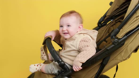 A happy child is sitting in a baby carriage on a studio yellow background. Smiling toddler baby boy