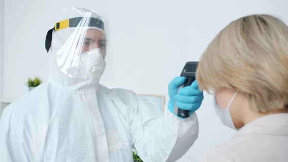 Doctor in Protective Costume Checking Body Temperature with Notouch Thermometer Examining Female alt