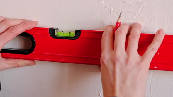 Drawing horizontal markings on the wall by level - DIY home repair. A woman in a red baseball cap an alt